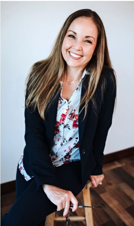 A woman in floral shirt and black jacket smiling.